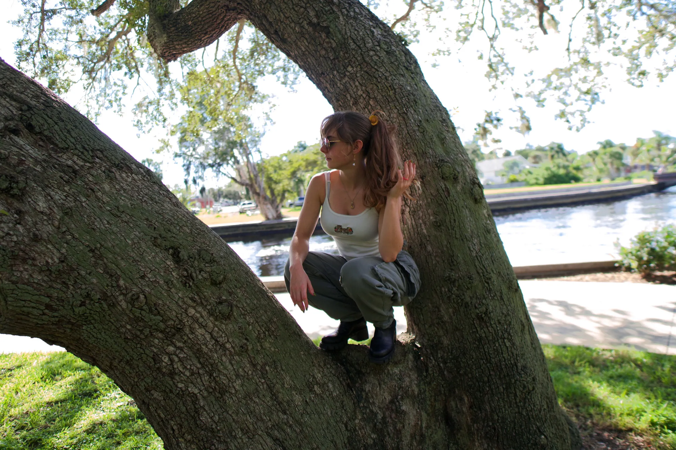 A woman crouched at the base of an oak, looking off to the side