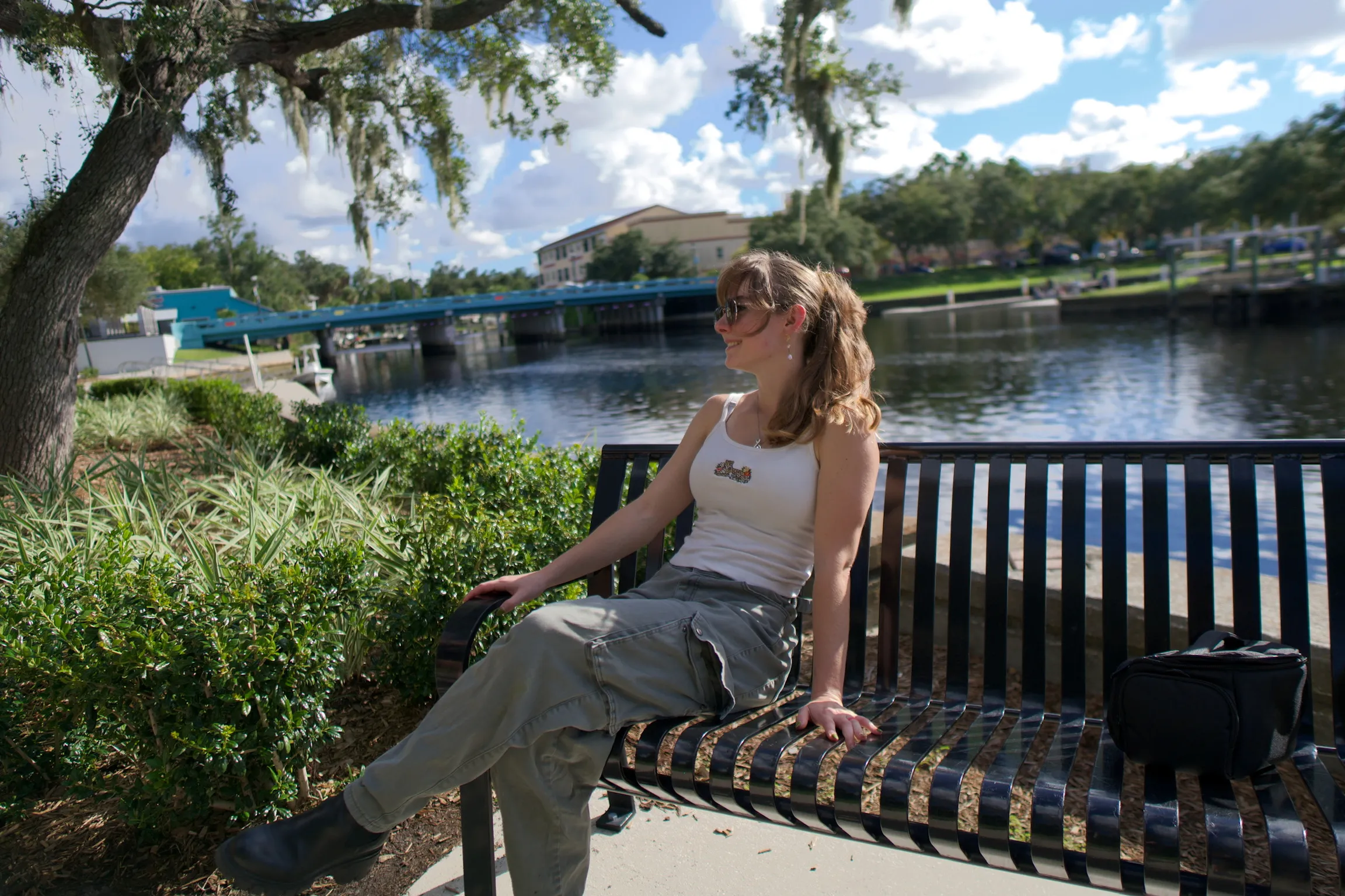 A woman on a waterside bench with one arm resting along the back