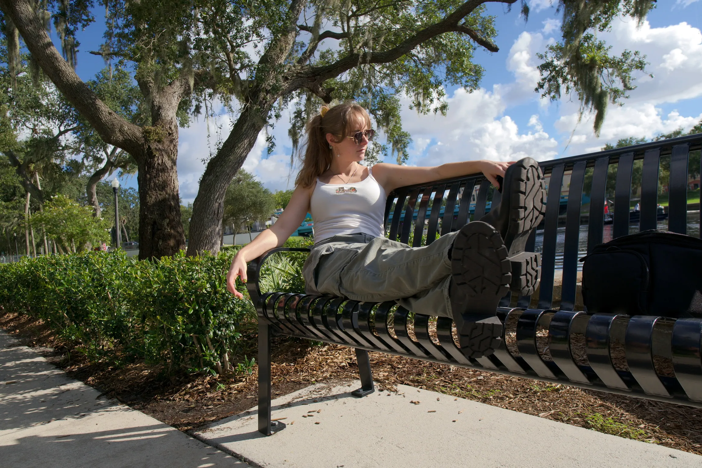 A woman lying across a metal bench with one boot up on the backrest