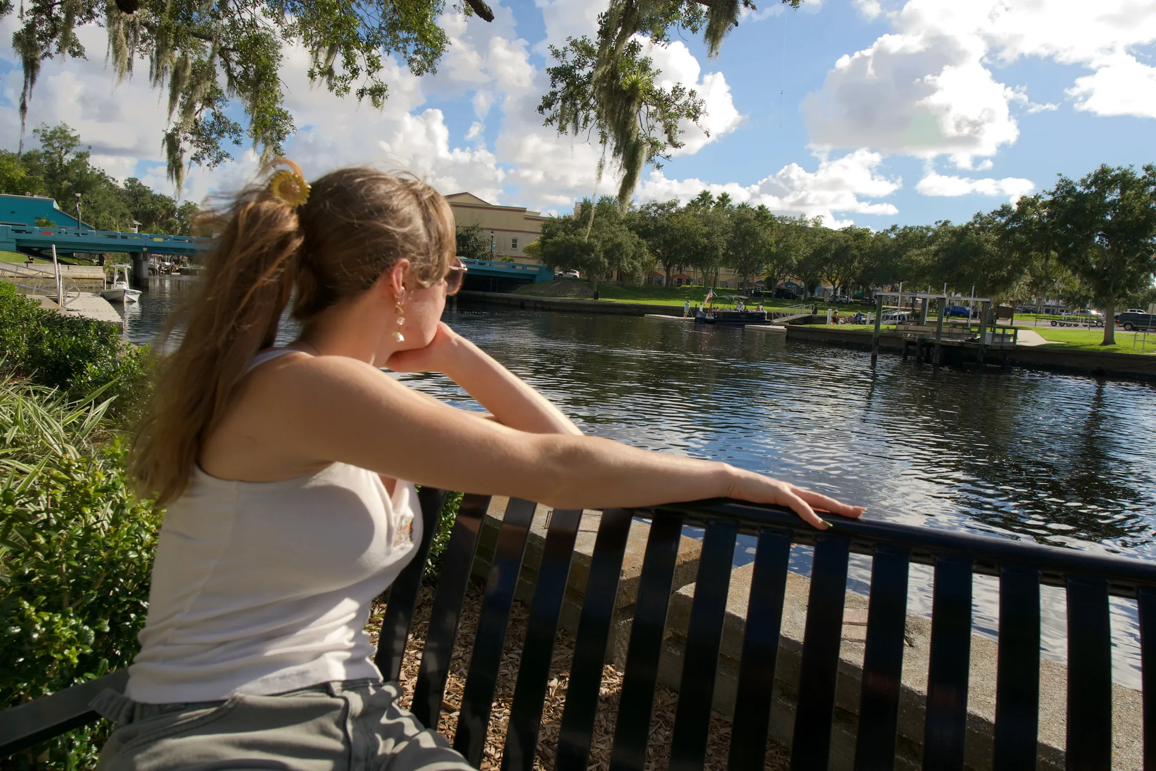 A woman seated on a bench from behind, arm along the rail, looking out over the water